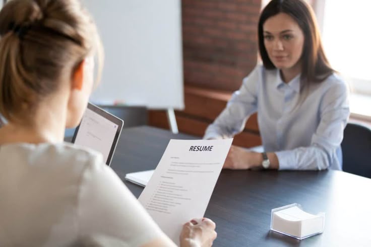 A job interview scene with a candidate sitting across the table from an interviewer who is holding a resume, illustrating a guide on how to ace your next job interview.